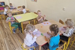 Dzieci malują farbami przy stolikach.