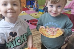 Chłopcy z uśmiechem wręczają skomponowaną własnoręczne zabawkową pizzę.