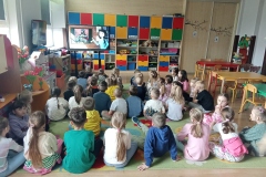 Dzieci siedzą na dywanie i oglądają film edukacyjny o chrzcie Polski.