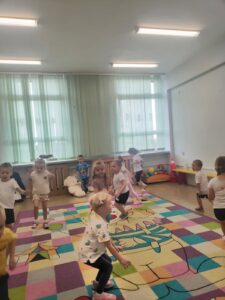 Motylki biorą udział w zabawie ruchowej na kolorowym dywanie. Są roześmiane i skupione na zadaniu.