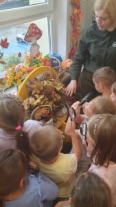 Dzieci trzymaja w ręku lupy. Badają budowę liści i słuchają pani z Kozienickiego Parku Krajobrazowego.