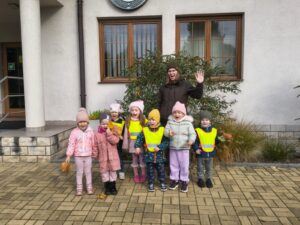 Dzieci z grupy Motylki pozują do wslnego zdjęcia. Towarzyszy im pani leśnik, machają do obiektywu.