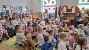 Przedszkolaki siedzą na dywanie, obserwują spektakl teatralny. Są zaciekawione.