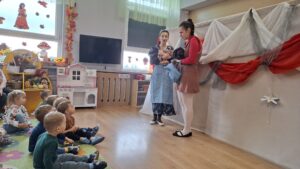 Aktorki teatralne odgrywają swoje role, dzieci siedzą przed nimi na dywanie i oglądają przedstawienie.
