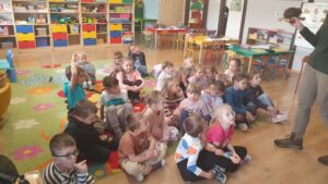 Dzieci siedzą na dywanie w sali przedszkolnej. Pani z Kozienickiego Parku Krajobrazowego pokazuje model jeża.