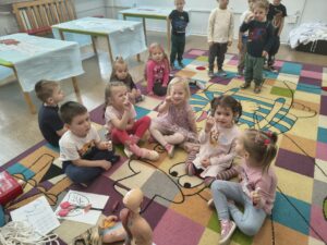 Dzieci siedza na dywanie. Pokazuję zagipsowane palce, uśmiechaja się do aparatu.