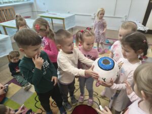 Dzieci stoją na dywanie i oglądaja model ludzkiego oka. Podaja go sobie z rąk do rąk.