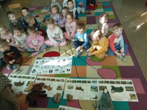 Dzieci siedzą na dywanie i zapoznają się ze zwierzętami i tropami, jakie zostawiają.