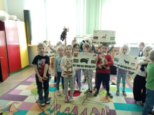 Dzieci pozują do zdjęcia, w rękach trzymają plansze edukacyjne i maskotki zwierząt.