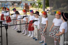 Na scenie dzieci z grupy Liski ubrane w białe koszulki śpiewają do mikrofonów. Chłopcy mają góralskie kapelusze a dziewczynki kwiaty we włosach i kwieciste spódniczki.