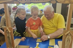 Dziewczynki z pomocą Pszczelarza rolują plaster wosku formując świecę.